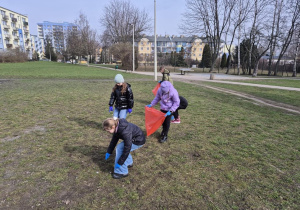 Uczniowie porządkują teren wokół szkoły. Zbierają śmieci do plastikowych worków.