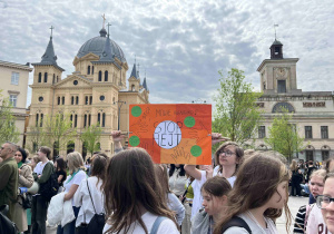 Uczniowie z klasy siódmej stoją na Placu Wolności z przygotowanym transparentem.