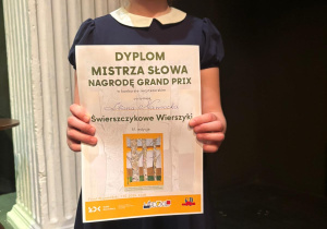 Uczennica klasy 2b trzyma w dłoni otrzymaną nagrodę Grand Prix w wojewódzkim konkursie recytatorskim – Świerszczykowe wierszyki.