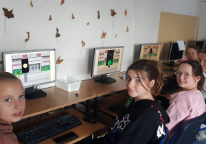 Informatyka. Programowanie sygnalizacji świetlnej, bezpieczna droga do szkoły. Prace uczniów klas 5b i 7a widoczne na ekranach komputerów.