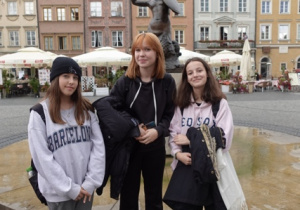 Trzy uczennice z klasy 8f stoją przy pomniku Warszawskiej Syrenki na Starym Mieście