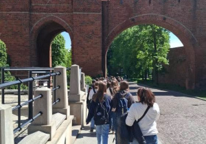 Uczniowie z przewodnikiem zwiedzają Toruń, przechodzą przez Bramę Miasta.
