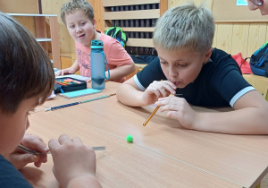 Uczniowie wykonują ćwiczenia oddechowe – „strzelają gole” dmuchając przez słomkę na piłeczkę.