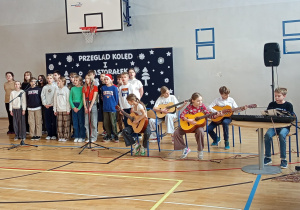 Dzieci z klasy 5d śpiewają i grają na instrumentach muzycznych kolędę – „Przybieżeli do Betlejem”.