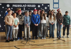 Uczniowie z klasy 6b podczas prezentacji na Sali gimnastycznej śpiewają kolędę – „Zaśpiewajmy Jezusowi dziś”.