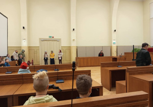 Dzieci przyglądają się pozorowanej rozprawie sądowej, w której pracownicy sądu wcielają się w zwierzęta.