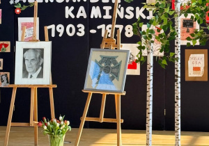 Dekoracja poświęcona pamięci Aleksandra Kamińskiego – tablica z pracami uczniów, wierzby, sztaluga z portretem Aleksandra Kamińskiego i sztaluga z Krzyżem harcerskim