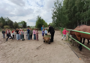 Pierwszaki stoją w rzędzie czekając na to żeby mogły nakarmić trawą konie.
