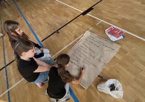 Uczniowie z klas 4 – 5 w trakcie apelu na dużym formacie papieru zapisują hasła przeciwko przemocy rówieśniczej