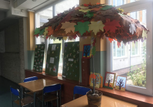 Parasol umieszczony w donicy. Góra wyklejona kolorowymi, papierowymi liśćmi.