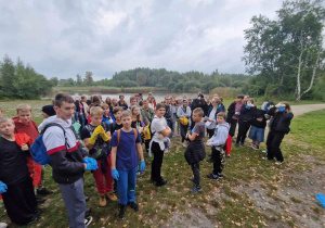 Uczniowie znajdują się na miejscu zbiórki. Na pierwszym planie widoczne worki z zebranymi przez uczniów śmieciami