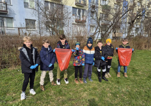 Uczniowie porządkują teren wokół szkoły. Zbierają śmieci do plastikowych worków.