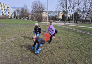 Uczniowie porządkują teren wokół szkoły. Zbierają śmieci do plastikowych worków.