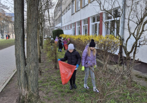 Uczniowie porządkują teren wokół szkoły. Zbierają śmieci do plastikowych worków.