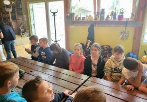 Uczniowie czekają na zajęcia , siedząc za dużym drewnianym stołem.