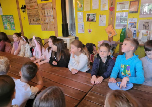 Uczniowie czekają na zajęcia , siedząc za dużym drewnianym stołem.