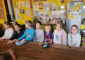 Uczniowie czekają na zajęcia , siedząc za dużym drewnianym stołem.