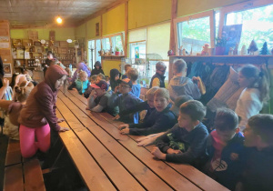 Uczniowie czekają na zajęcia , siedząc za dużym drewnianym stołem.