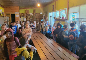 Uczniowie czekają na zajęcia , siedząc za dużym drewnianym stołem.