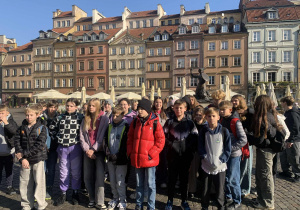 Uczniowie stoją przy Pomniku Syrenki na Starym Mieście w Warszawie.