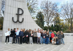 Uczestnicy wycieczki do Warszawy stoją przy Pomniku Armii Krajowej i Polskiego Państwa Podziemnego.