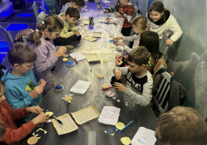 Dzieci siedzą przy stole i uczestniczą w grupowych zajęciach.