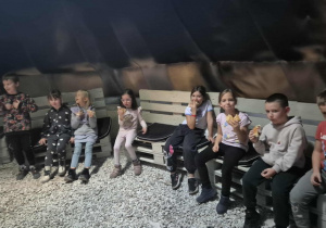 Dzieci siedzą przy ognisku jedząc poczęstunek.