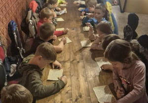 Dzieci siedzą przy stole i uczestniczą w grupowych zajęciach.