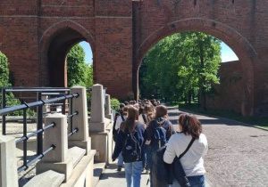 Uczniowie z przewodnikiem zwiedzają Toruń, przechodzą przez Bramę Miasta.