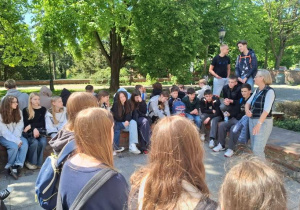 Uczniowie siedząc na murach obronnych Torunia słuchają legendy miasta.