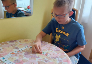 Zajęcia logopedyczne - uczeń gra w domino logopedyczne, służące utrwalaniu głosek sz, ż/rz, cz, dż
