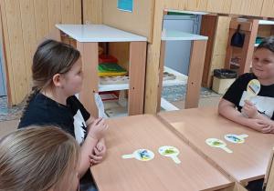 Dziewczynki wykonują ćwiczenia artykulacyjne z wykorzystaniem lizaków logopedycznych. Dzieci powtarzają wyrazy dźwiękonaśladowcze