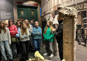 Uczniowie przebywają na parterze Muzeum Powstania, słuchają przewodnika, który opowiada o czasie okupacji i wybuchu Powstania.