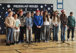 Uczniowie z klasy 6b podczas prezentacji na Sali gimnastycznej śpiewają kolędę – „Zaśpiewajmy Jezusowi dziś”.