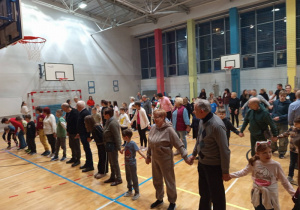 Dzieci i ich Babci i Dziadkowie w drużynach przechodzą przez koło hula-hop bez używania rąk.