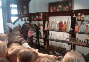 Pierwszaki oglądają stare wagi apteczne, oglądają naczynia, w których przechowywano lekarstwa. Farmaceuta opowiada im o tym jak wyglądał ten zawód dawniej