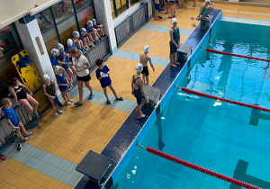 Młodzi pływacy szykują się przy basenie do zaprezentowania swoich umiejętności pływackich