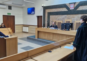Widok na salę rozpraw, przesłuchiwanego świadka, sędziego i prokuratora.
