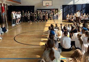 Apel z okazji Święta Patrona Szkoły – uczniowie i nauczyciele zgromadzeni na sali gimnastycznej.