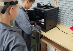 Uczeń zdejmuje z platformy drukarki 3D gotowe elementy obudowy.