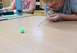 Uczniowie wykonują ćwiczenia oddechowe – „strzelają gole” dmuchając przez słomkę na piłeczkę