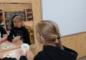 Dziewczynki wykonują ćwiczenia artykulacyjne z wykorzystaniem lizaków logopedycznych. Dzieci powtarzają wyrazy dźwiękonaśladowcze.